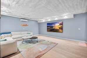 Ein modernes Wohnzimmer mit weißer Decke, einem großen Gemälde eines Sonnenuntergangs, einem weißen Sofa und einem Couchtisch.