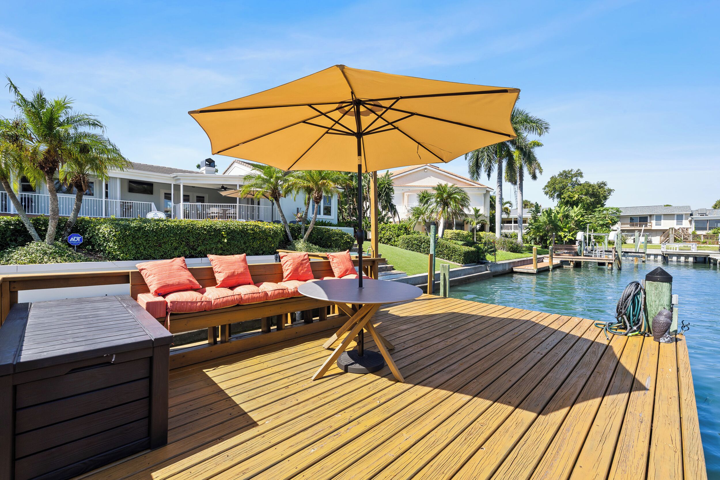 Une terrasse en bois avec une table et un canapé, un parasol jaune et, au fond, une étendue d’eau.