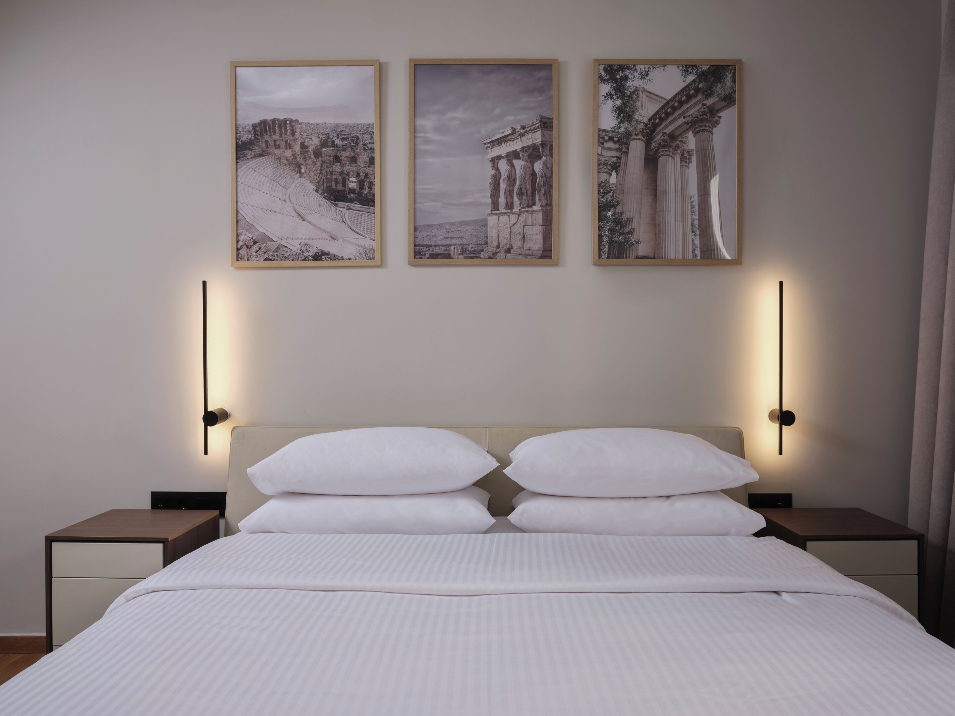 A hotel room with a bed, two bedside tables, and three framed pictures on the wall.