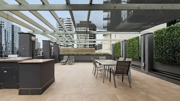En takterrass med ett område för utomhusmatlagning, ett utomhuskök och utsikt över de omgivande byggnaderna.