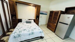 A bedroom with a bed, wooden wardrobe, and a refrigerator. - Charming Studio in the Heart of Bucerias. Great Vibe. Great Price! (Bucerías)