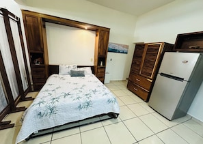 Quarto com cama, guarda-roupa de madeira e frigorífico.