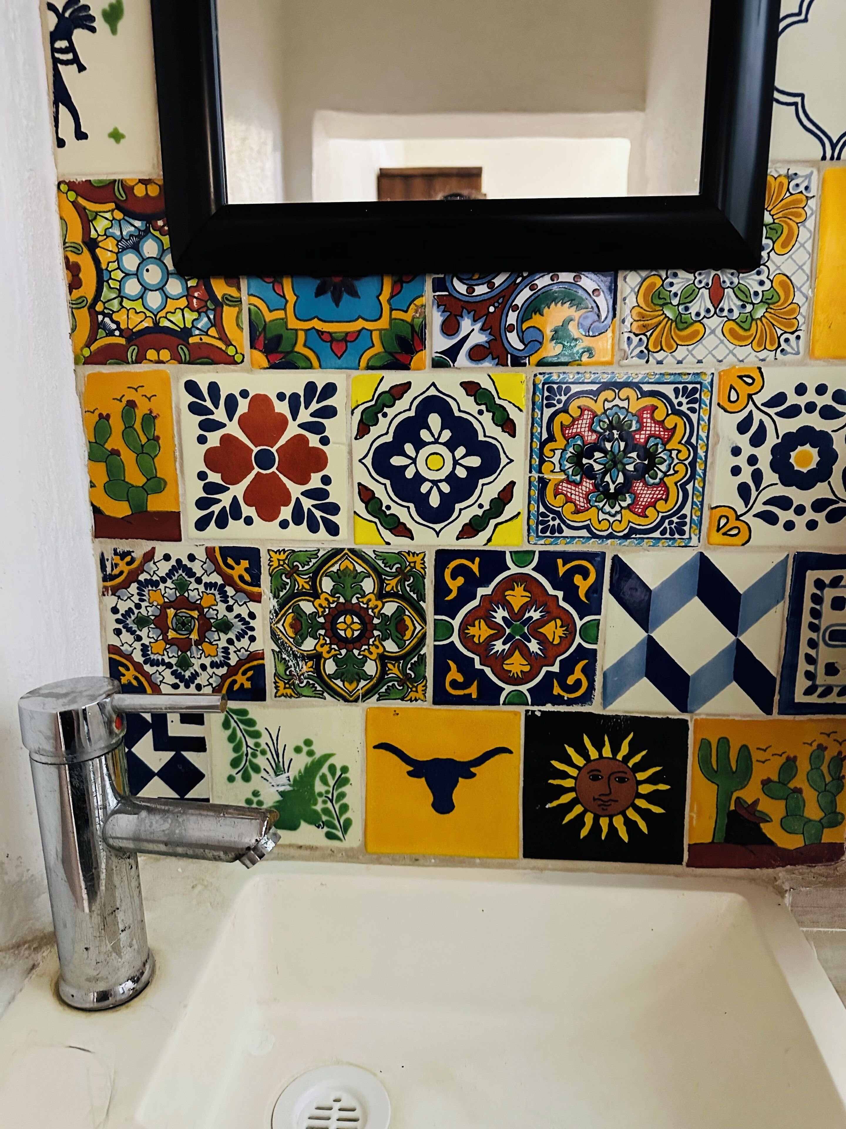 A bathroom with a sink, a mirror, and a wall decorated with colorful tiles.
