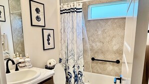 Un baño con lavamanos, inodoro y bañera. Hay cuadros en la pared y una cortina de ducha con diseño de árboles.