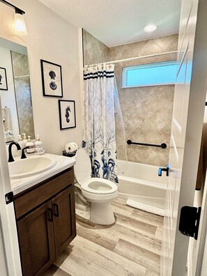 A bathroom with a sink, toilet, and bathtub. There are framed pictures on the wall and a shower curtain with a tree design. - 5 Minutes from Brownwood Square! 3Br, 2Ba, 6 Guest (The Villages)
