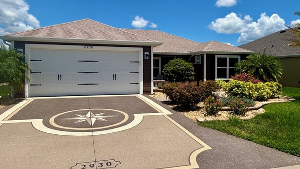 Una casa residencial con un garaje número 2930, un camino de entrada con un diseño de brújula y un césped bien cuidado con diversos arbustos y una palmera.