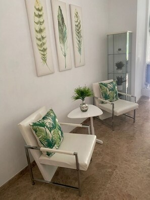 A seating area with a white sofa and chairs, a small round table, and a glass cabinet with plants. - The Golf View Marbella, a peaceful golf retreat in Guadalmina (San Pedro Alcántara)