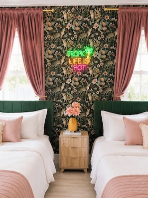 Ein Zimmer mit zwei Betten, einer Neonreklame und floralem Wandpapier.