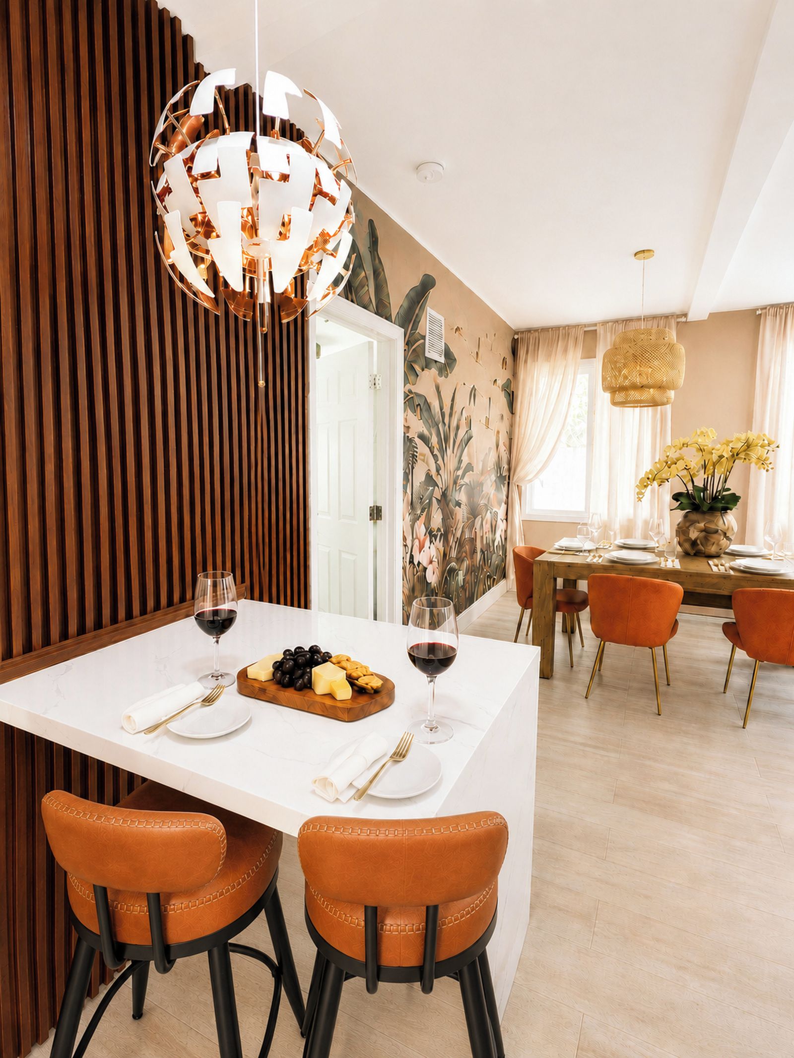 A modern dining area with a white table, two orange chairs, and a decorative pendant light.