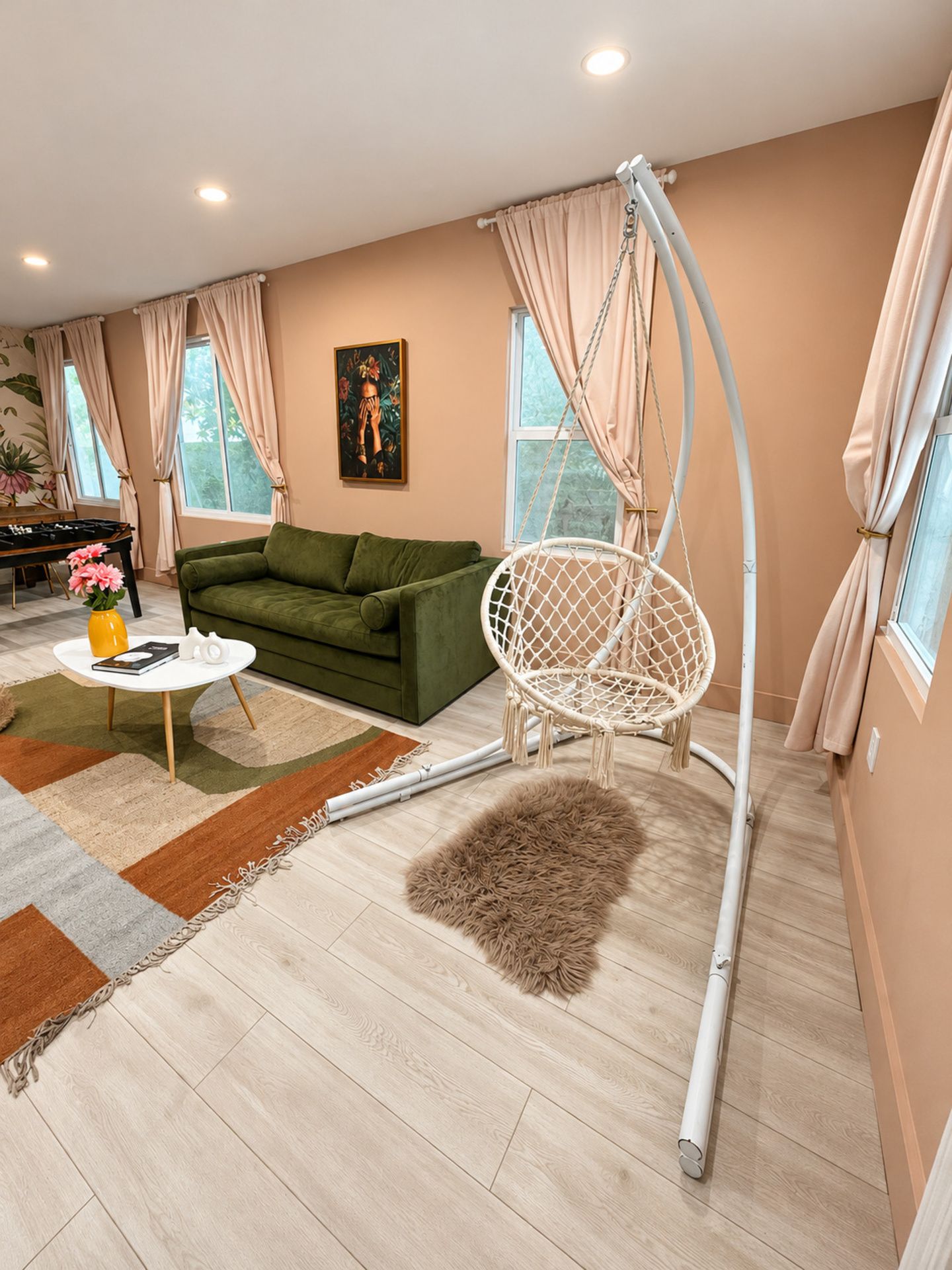 Ein Wohnzimmer mit einem grünen Sofa, einem weißen Hängesessel, einem kleinen Tisch mit einer Vase und einem Gemälde an der Wand.