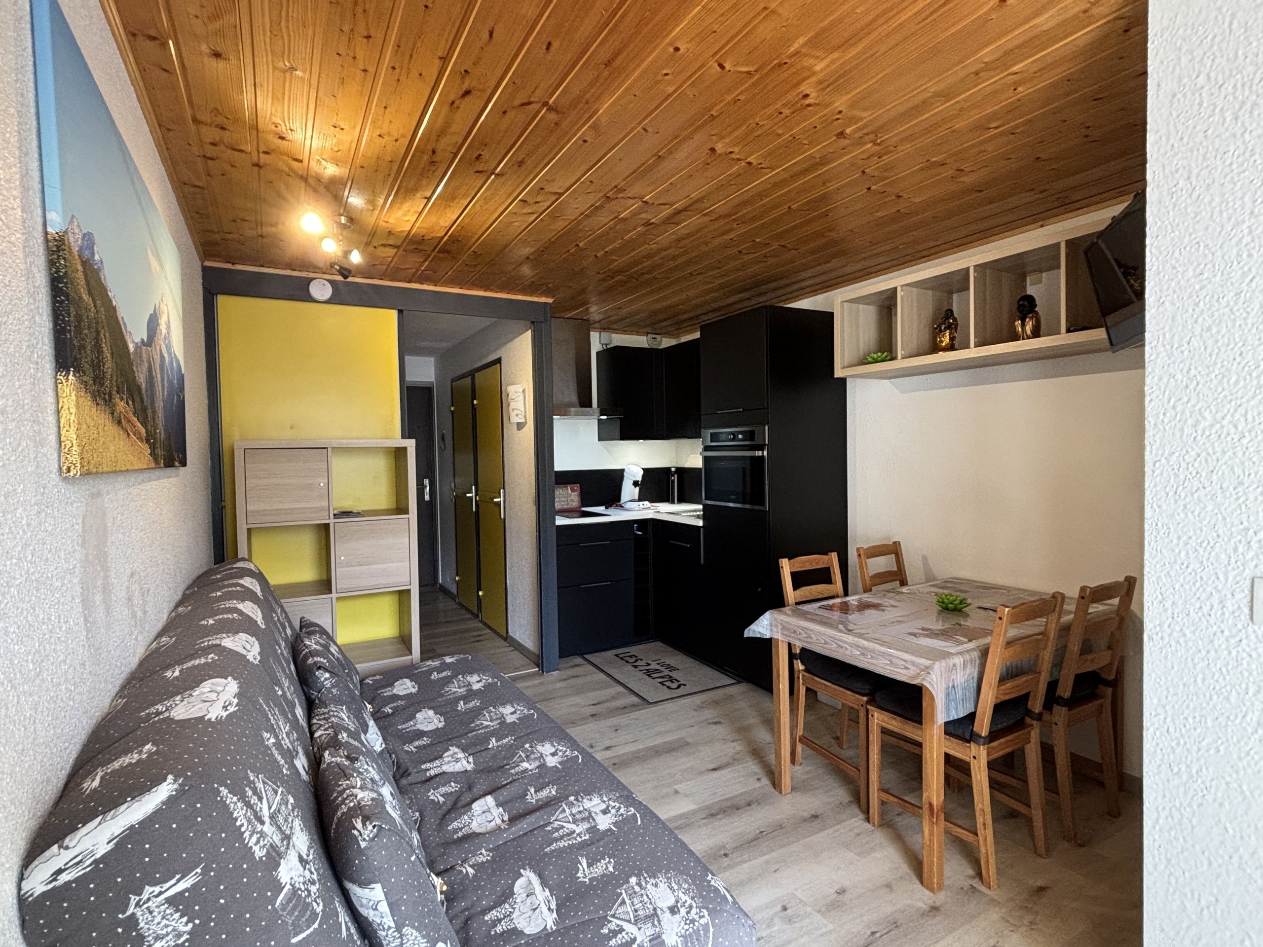Un espace de vie compact comprenant un canapé, une table à manger, des chaises, un coin cuisine et un couloir menant à une porte.