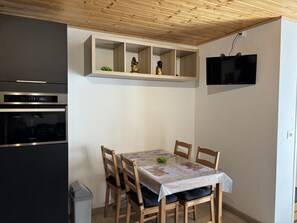 Eine Küche mit Einbauofen, einem Esstisch mit Stühlen und einem an der Wand befestigten Fernseher.