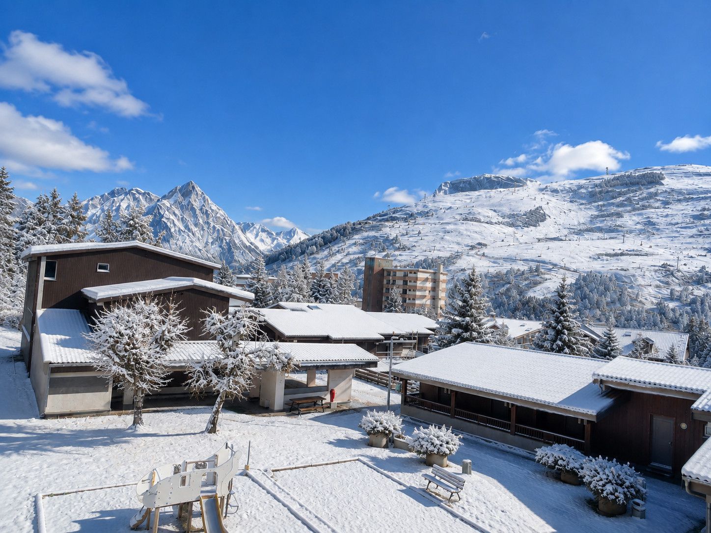 Une station de montagne enneigée, avec des bâtiments, une piste de ski et un ciel bleu dégagé.