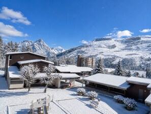 Ein schneebedecktes Bergresort mit Gebäuden, einer Skipiste und blauem Himmel.