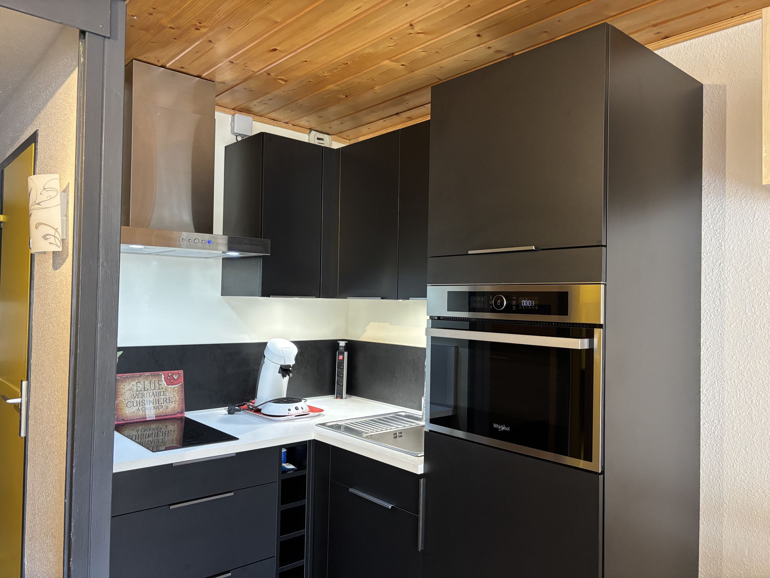 Una cocina moderna con armarios negros, una campana extractora de acero inoxidable, un horno integrado y una encimera con una cafetera.