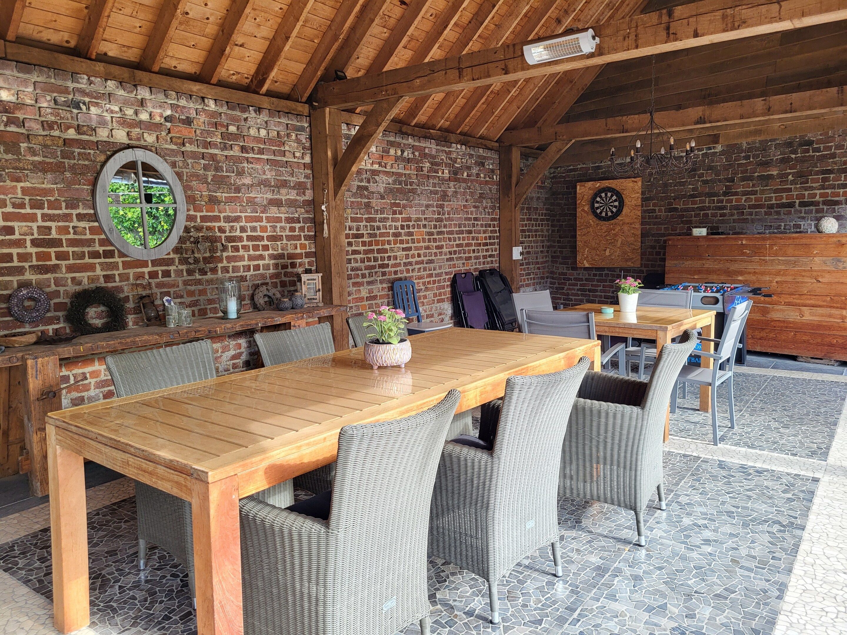 An outdoor dining area with a brick wall, wooden beams, and a dartboard.