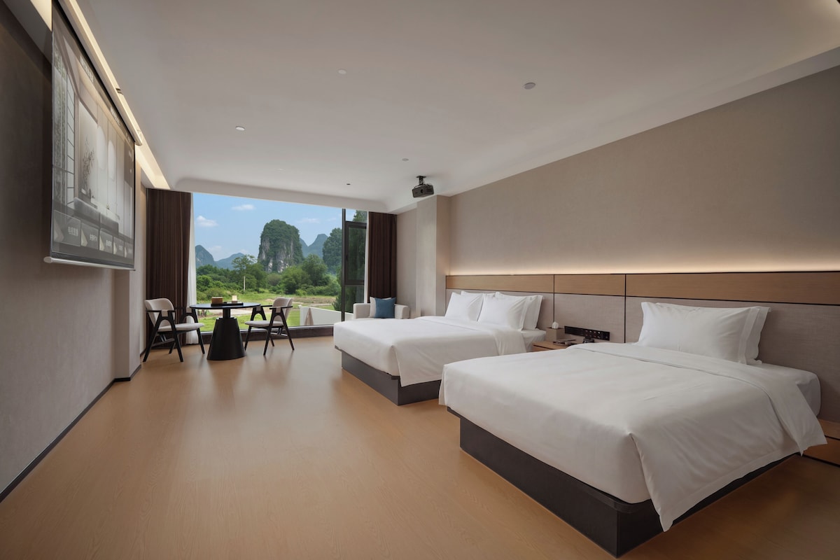 A hotel room with two beds, a dining table, and a view of the outdoors.