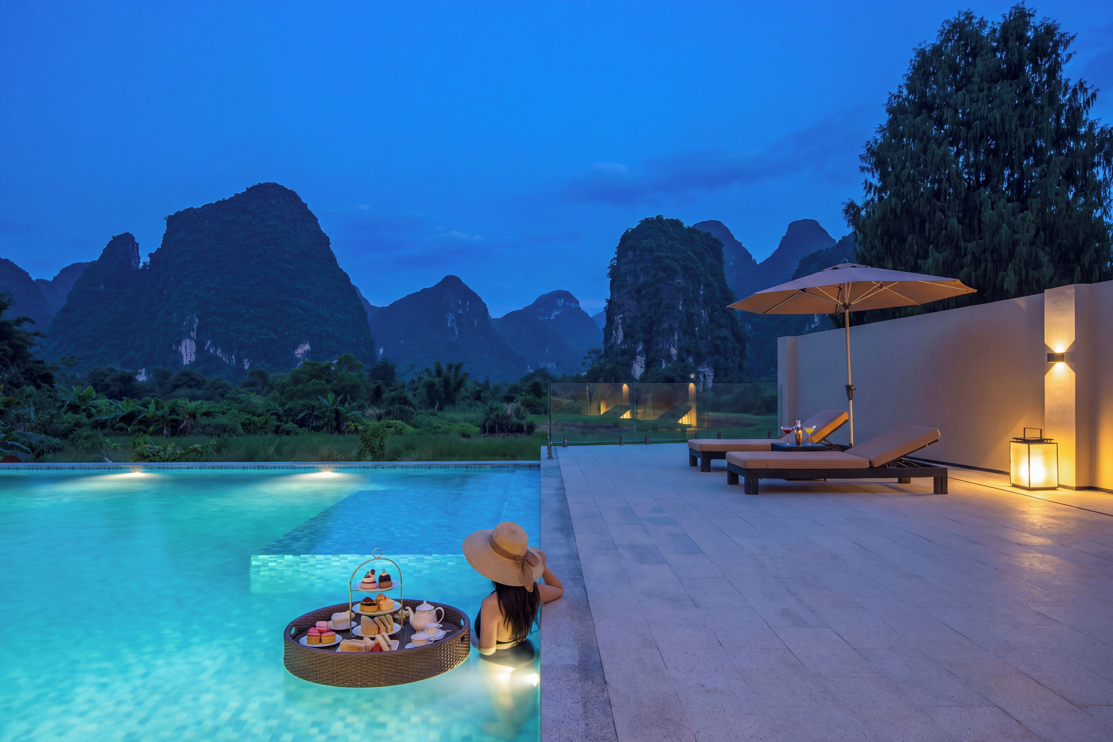 A poolside area with lounge chairs, a table with a drink tray, and a view of mountains.