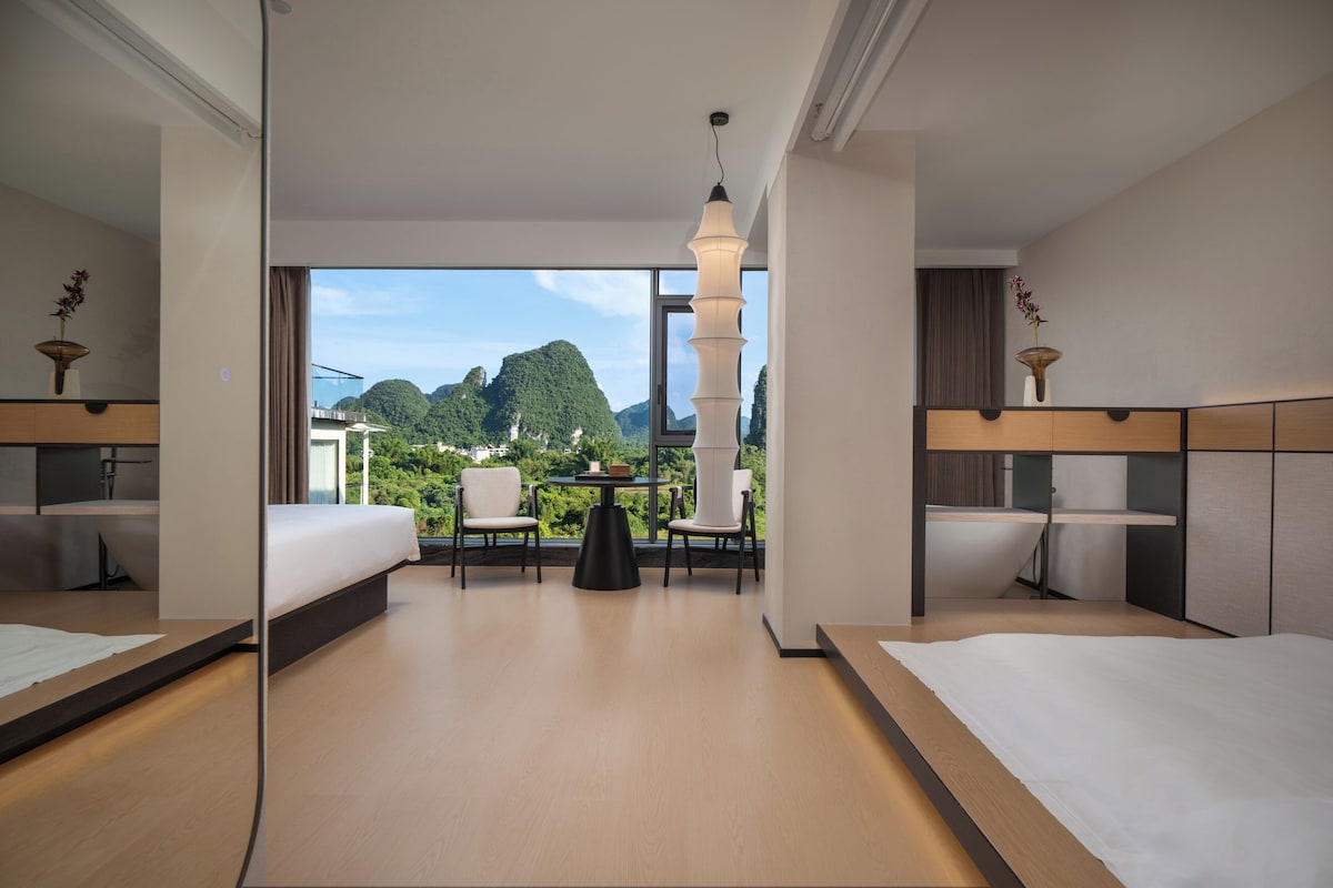 A hotel room with a large window, a bed, a desk, a chair, and a table.