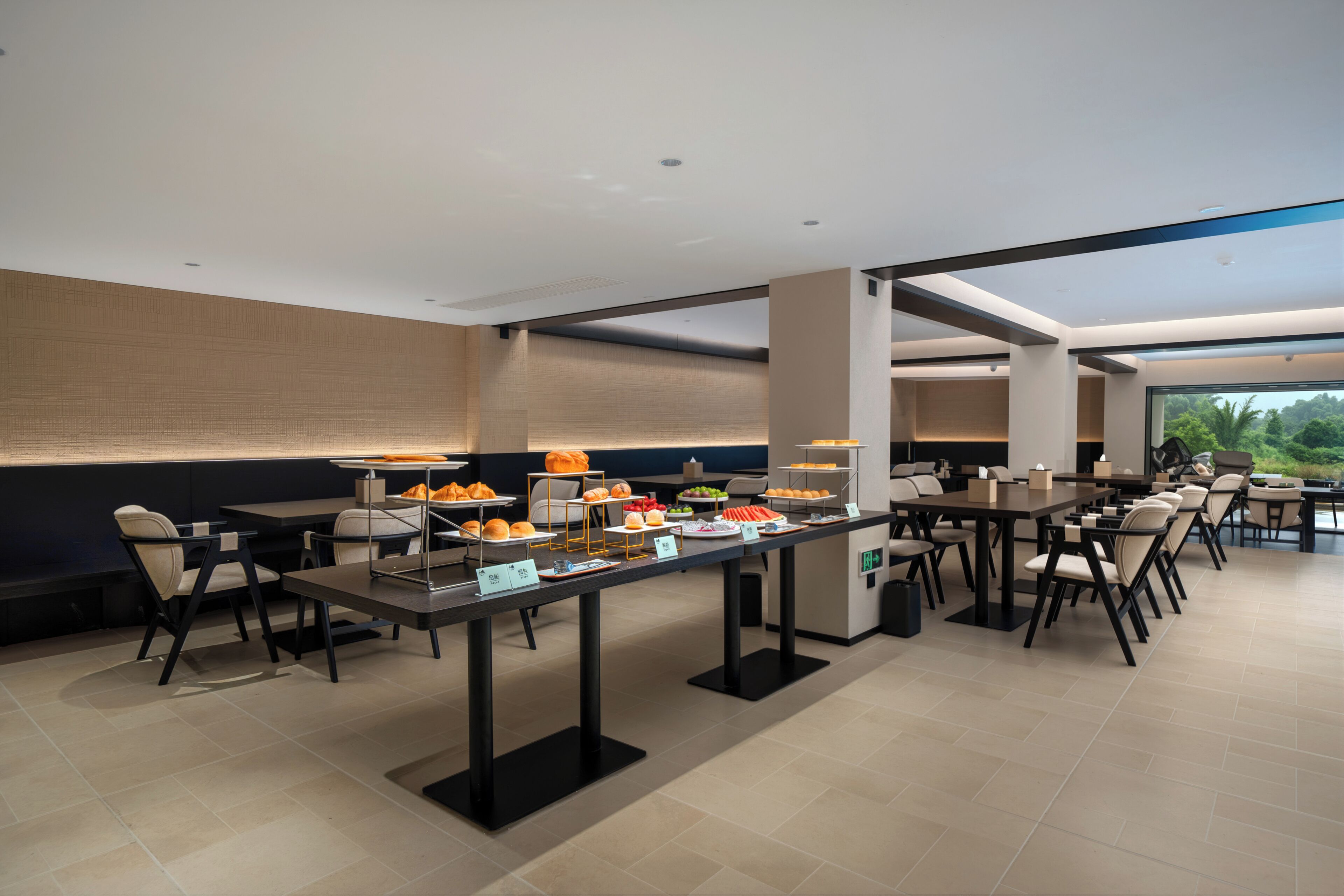 A modern dining area with multiple tables and chairs, a buffet setup with various food items, and a view of greenery outside.