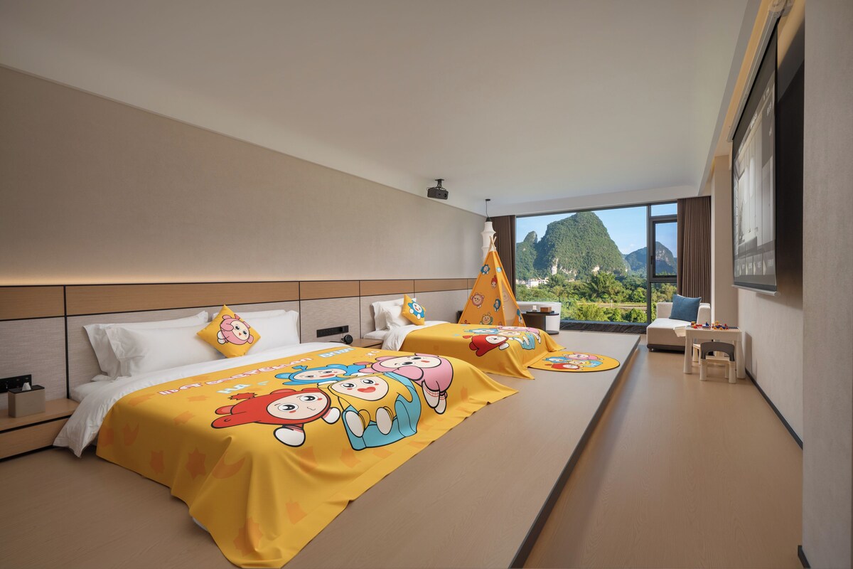 A hotel room with two beds, a large window with a mountain view, a small table with toys, and a TV.