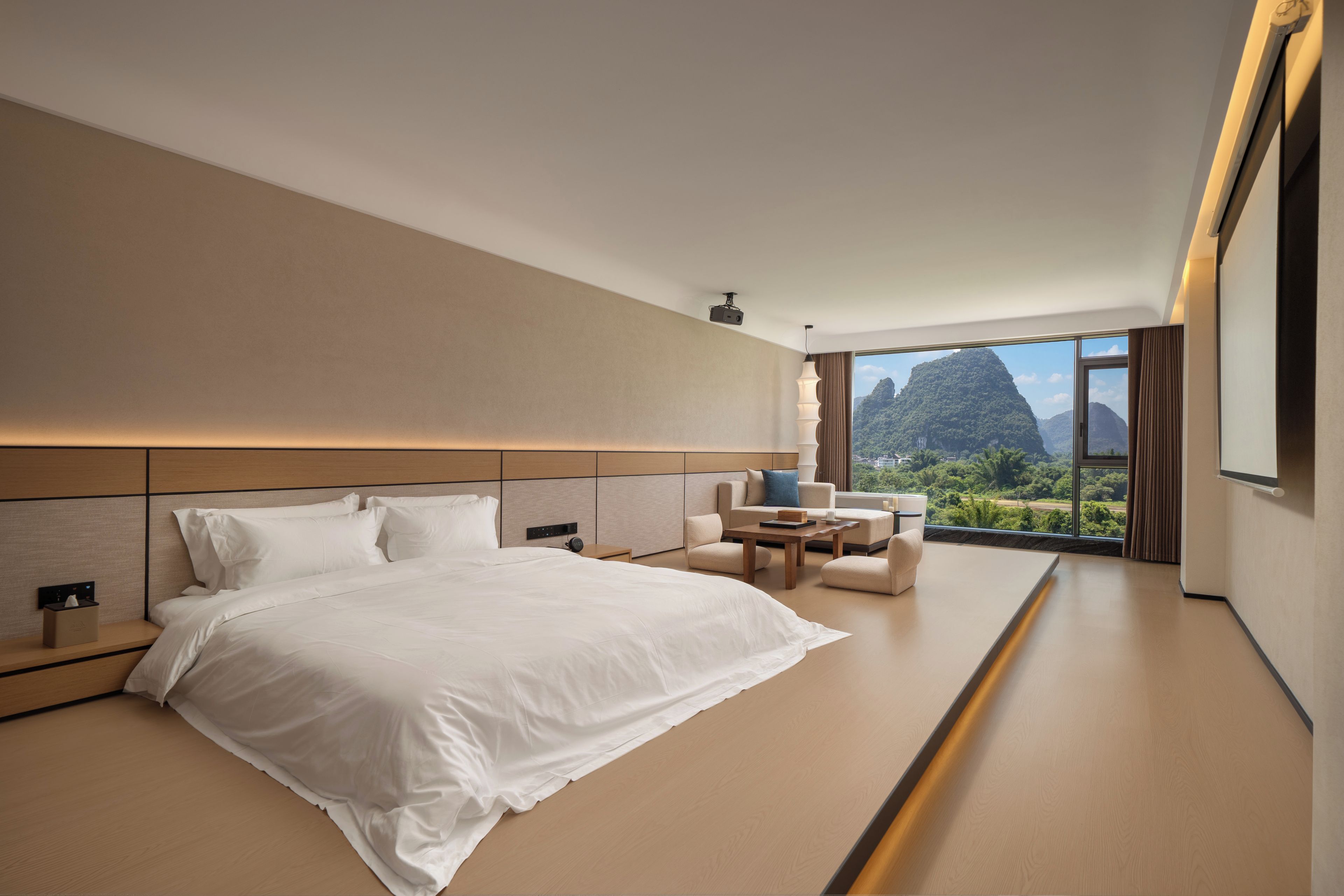Habitación de hotel moderna con una cama grande, zona de estar con una mesa y vistas a un paisaje montañoso.