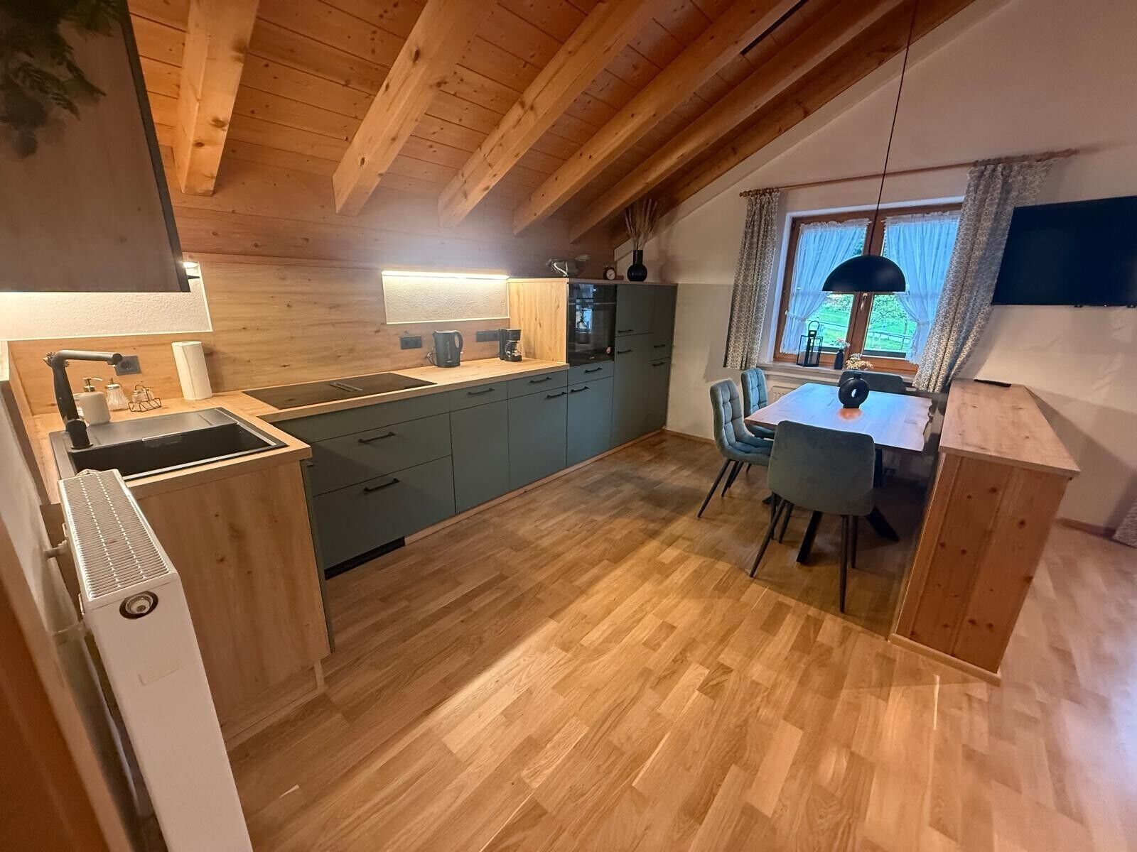A compact kitchen with a wooden ceiling, a dining area with a table and chairs, and a window with curtains.