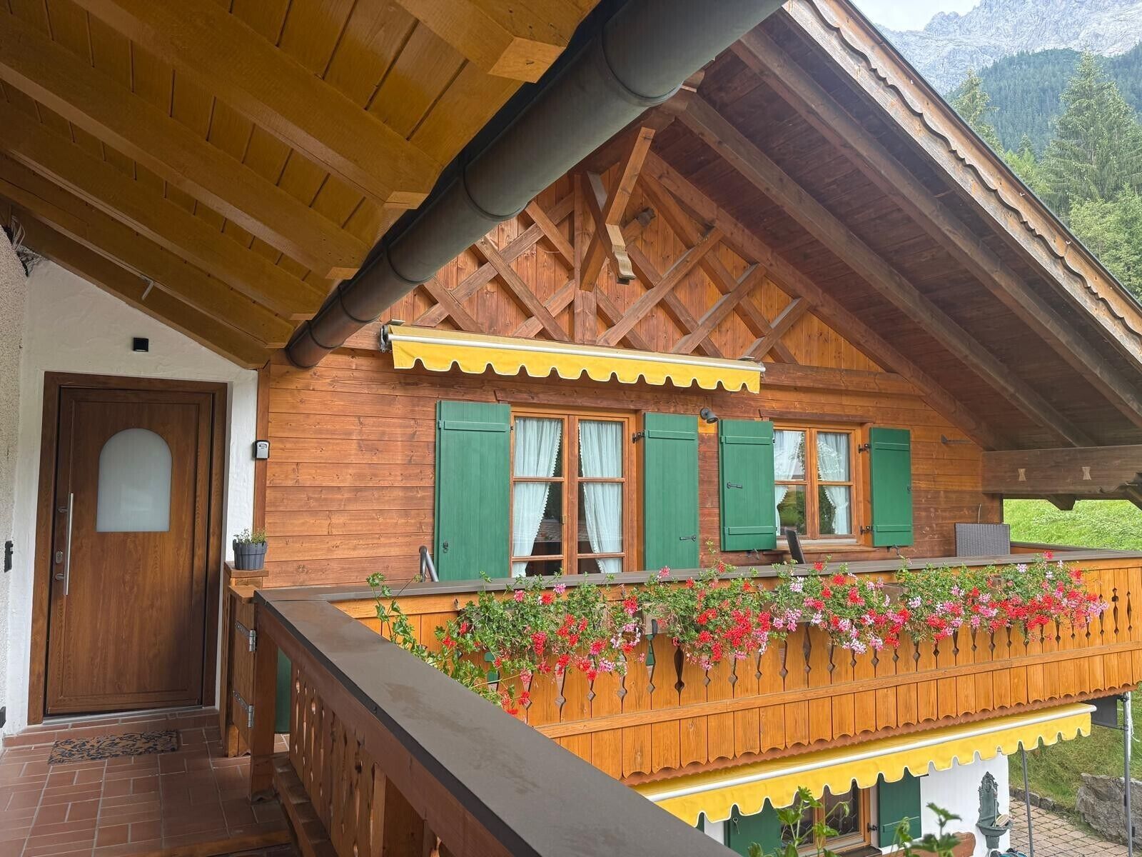 Eine Holzchalet mit Balkon, verziert mit Blumen, einer Holztür und einem Fenster mit grünen Rollläden.