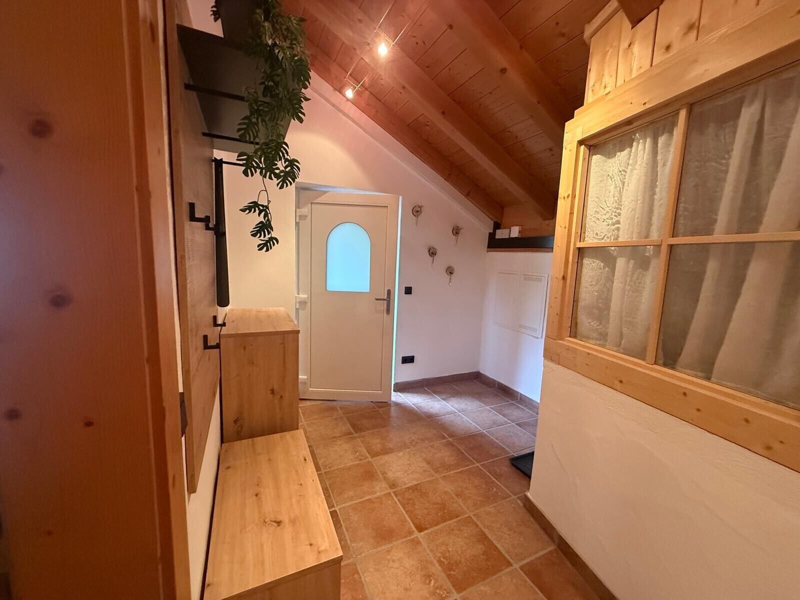 A narrow hallway with wooden walls and a sloped ceiling. A wooden bench is placed against the wall, and a door with a frosted glass panel is visible.