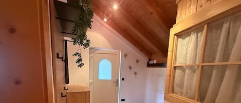 A narrow hallway with wooden walls and a sloped ceiling. A wooden bench is placed against the wall, and a door with a frosted glass panel is visible.