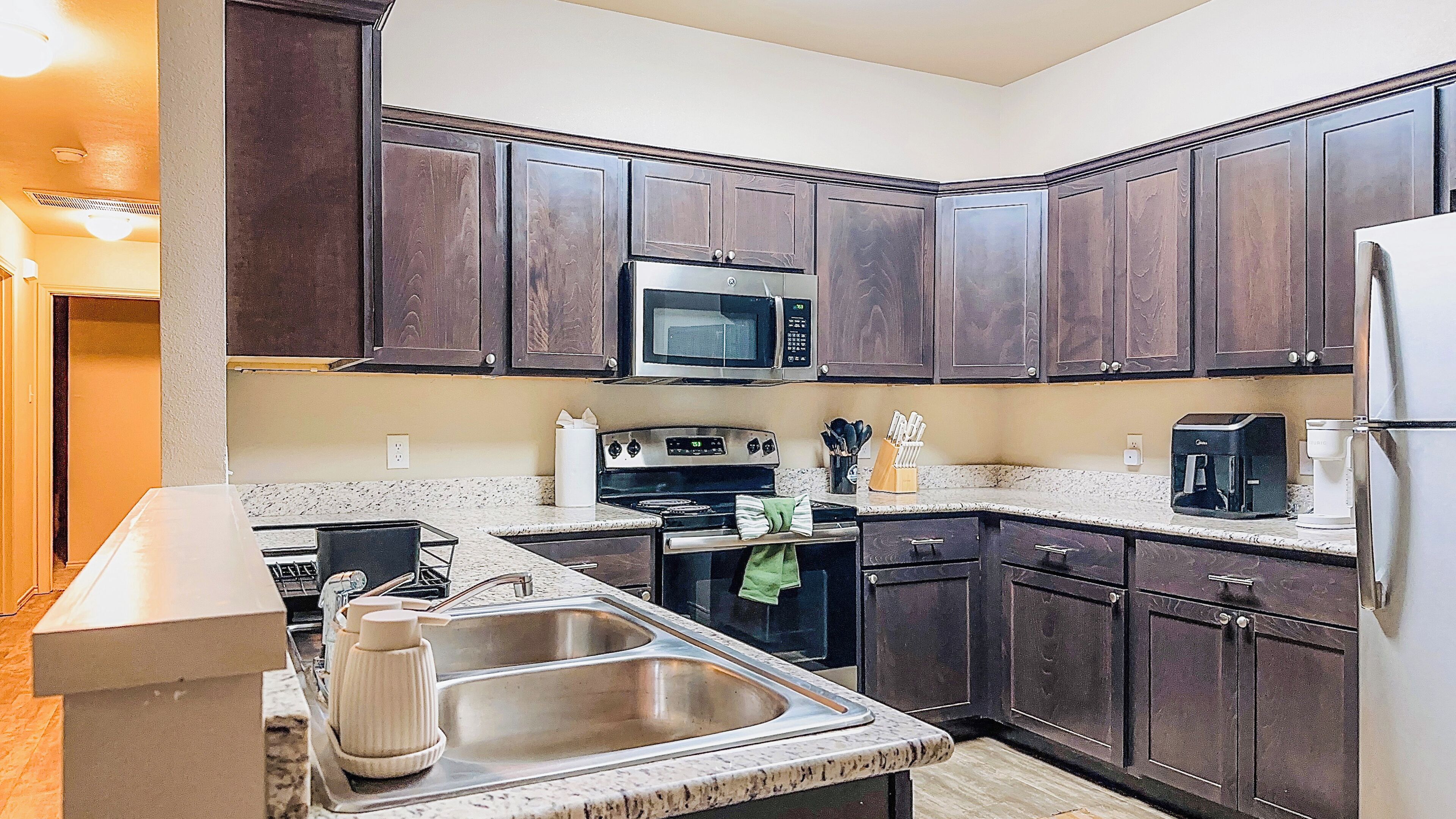 A kitchen with dark wood cabinets, a stainless steel sink, a microwave, a stove, and a refrigerator.