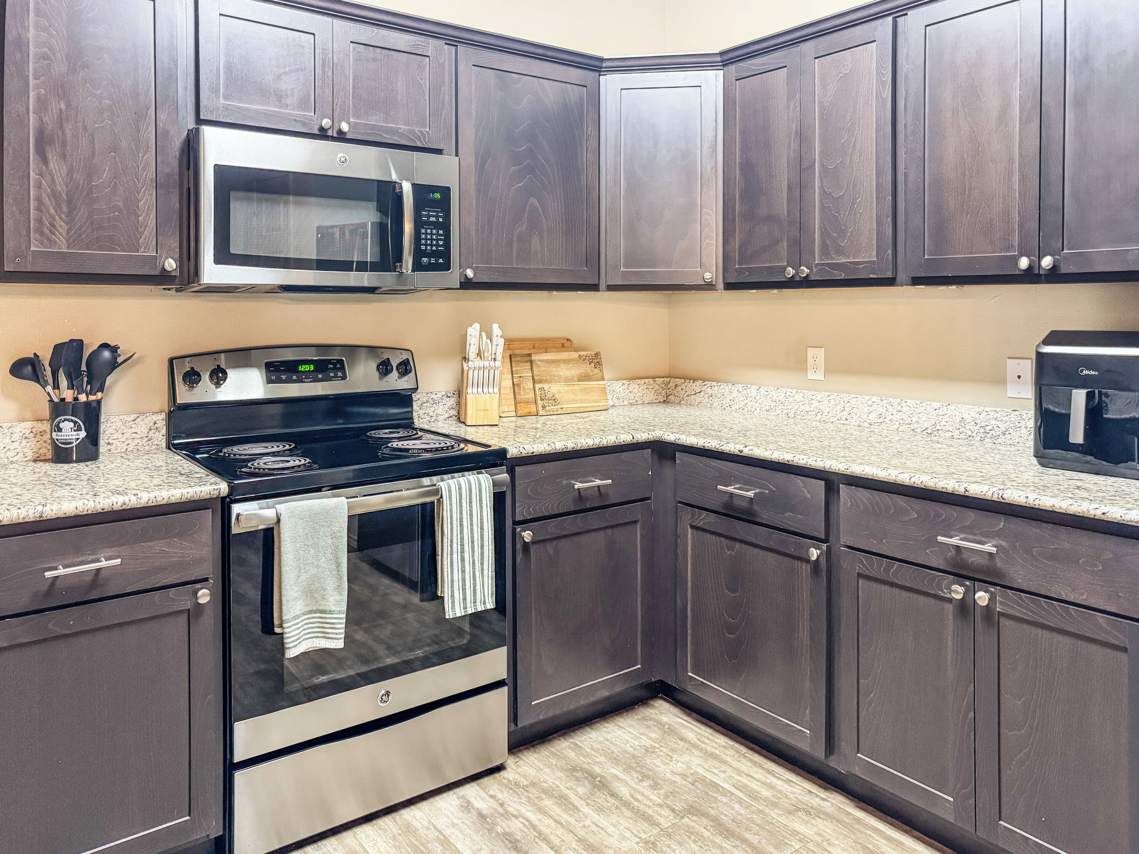 A kitchen with dark wood cabinets, a stainless steel stove, a microwave, and granite countertops.