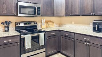 A kitchen with dark wood cabinets, a stainless steel stove, a microwave, and granite countertops.