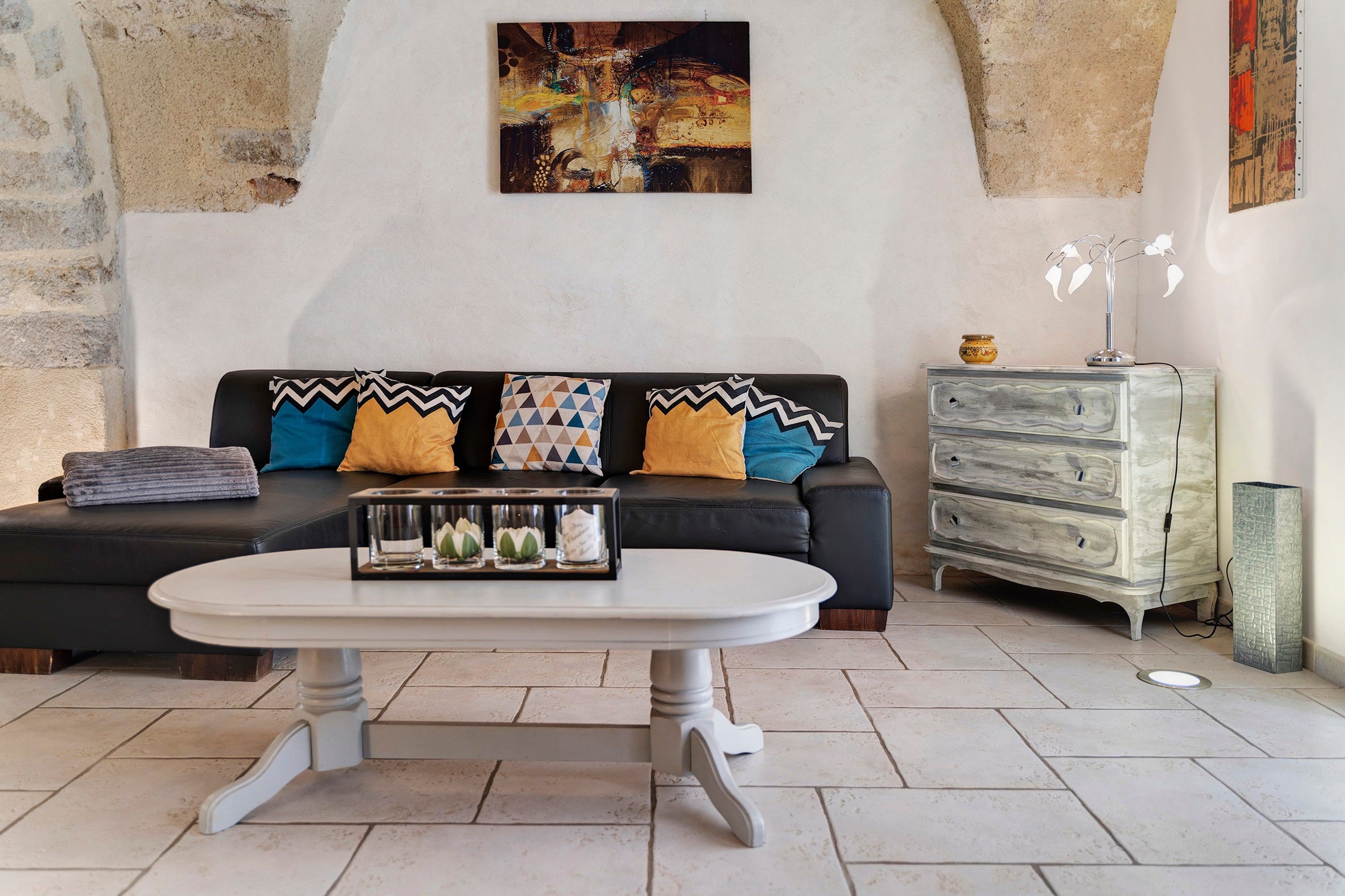 Ein Wohnzimmer mit schwarzem Sofa, gemusterten Kissen, einem weißen Couchtisch und einer dekorativen Vase.