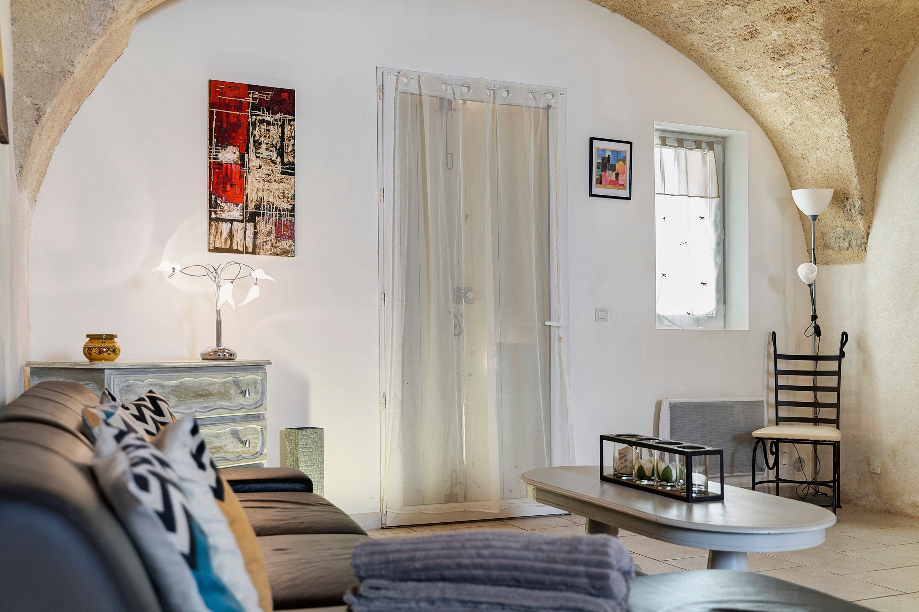 Sala de estar com sofá, mesa, cadeira, abajur e um quadro na parede.