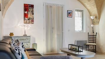 Sala de estar com sofá, mesa, cadeira, abajur e um quadro na parede.