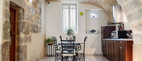 A cozy room with a stone wall, a wooden door, a dining table with chairs, a small potted plant, and a kitchenette with a microwave and coffee maker.