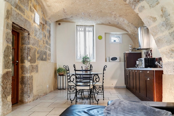 A cozy kitchen with a dining area, stone walls, a wooden door, and a window with curtains.