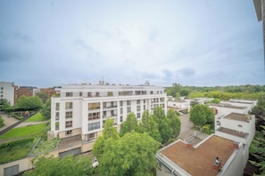 Un edificio de varios pisos con techo plano, rodeado de vegetación y otros edificios.
