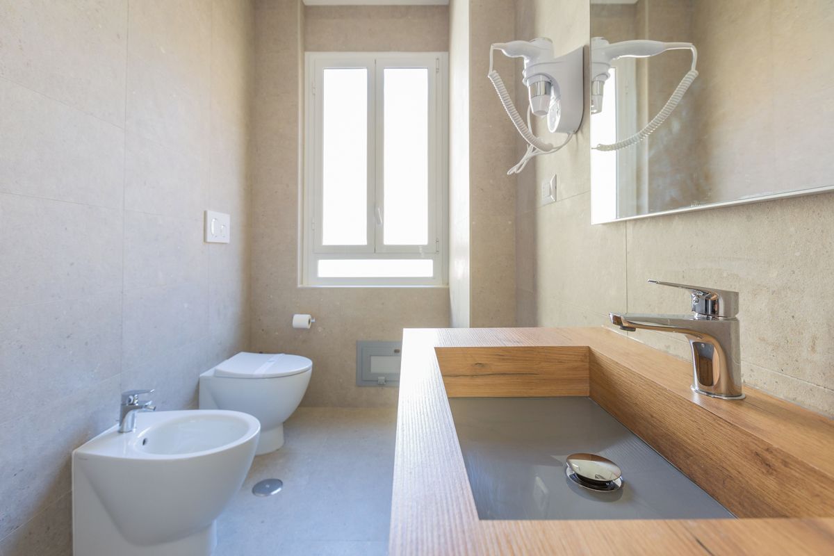 A modern bathroom with a bidet, a toilet, and a sink with a wooden countertop.