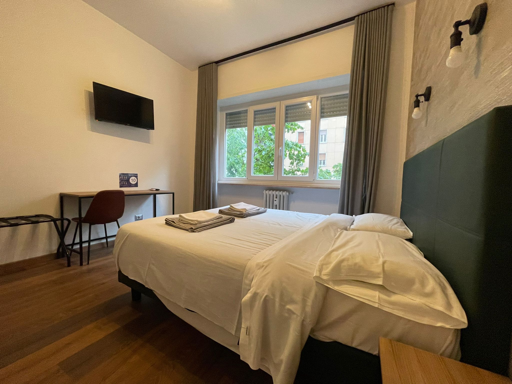 A hotel room with a bed, a desk, a chair, a TV, and a window with curtains.