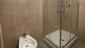 A bathroom with a glass-enclosed shower, a white bidet, and beige tiles.