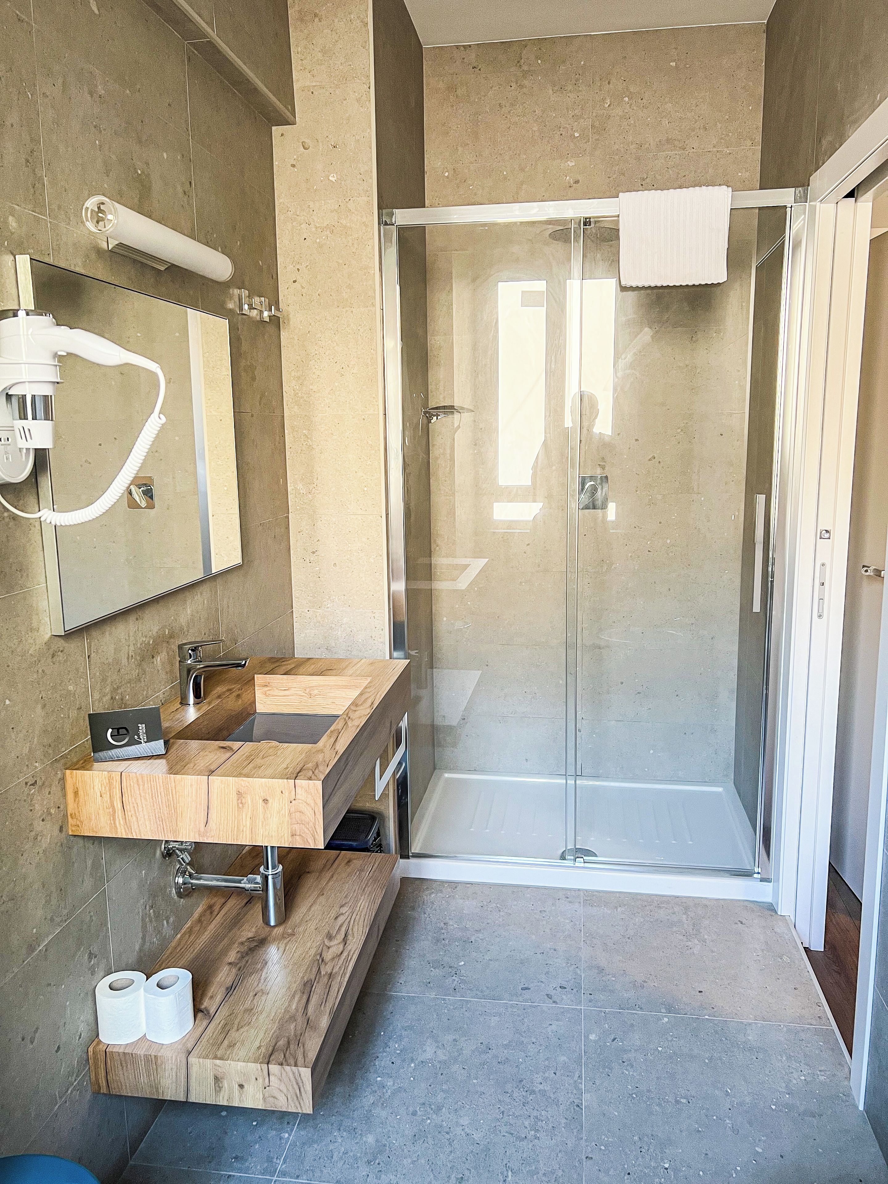 Un baño moderno con tocador de madera, cabina de ducha de vidrio y un espejo grande.