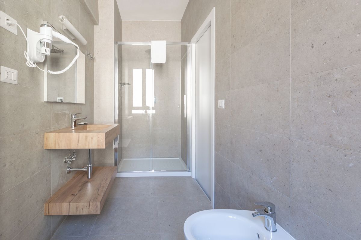 A modern bathroom with a wooden vanity, a glass shower enclosure, and a white sink.