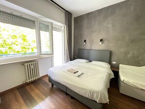 Un dormitorio moderno con una cama grande, un radiador, una ventana con cortinas y una pared gris con textura.
