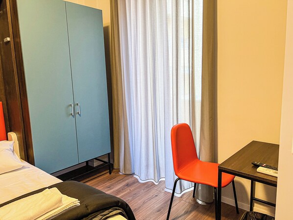 Una habitación de hotel con cama, escritorio, silla, armario y ventana con cortinas.