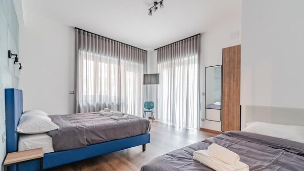A modern hotel room with two beds, a flat-screen TV, and a large window with curtains.
