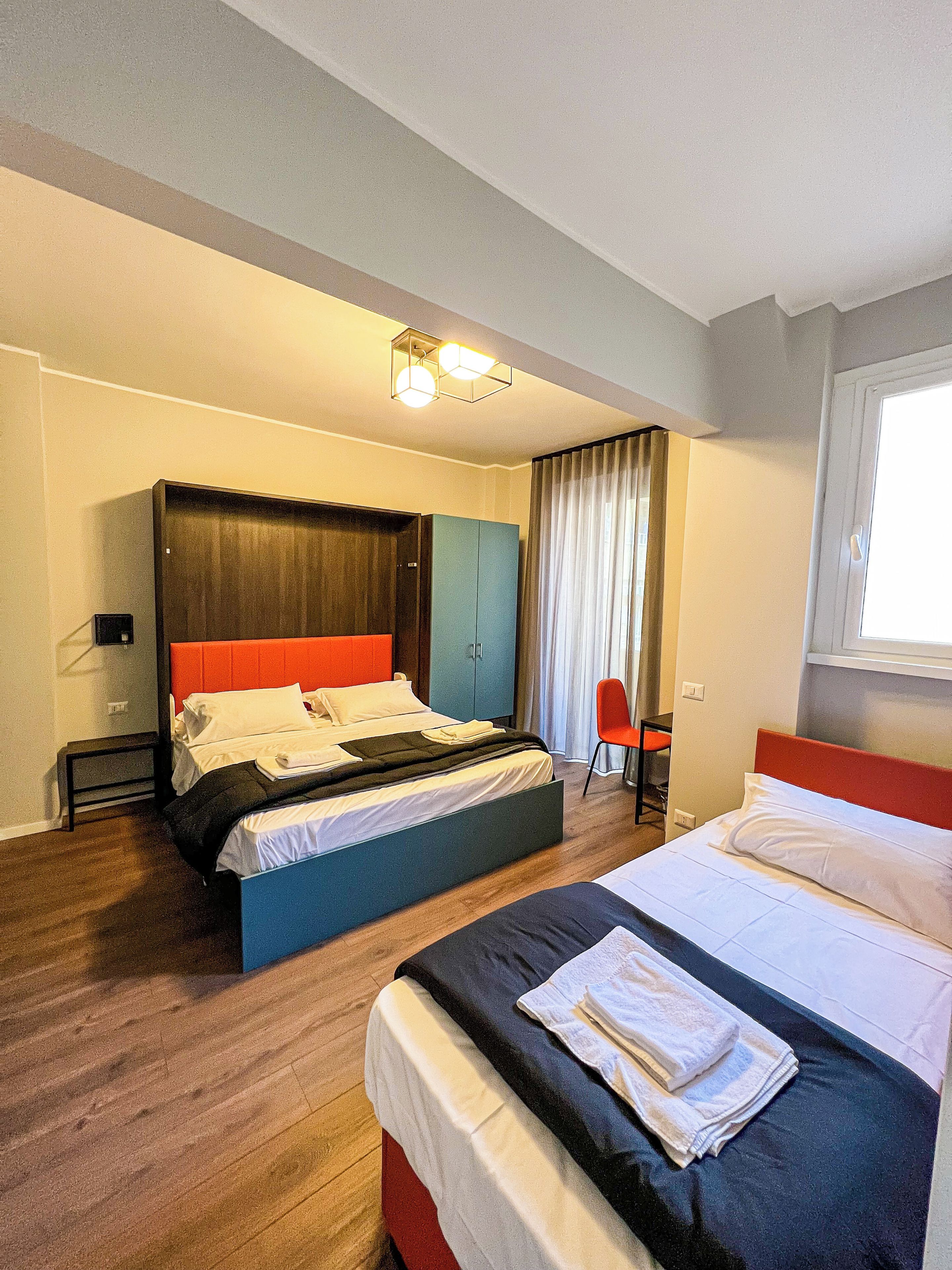 Ein Hotelzimmer mit zwei Betten, einem Kleiderschrank, einem Schreibtisch und einem Stuhl.