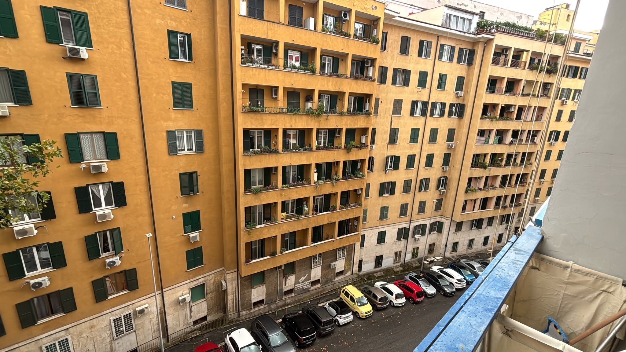 Un edifici residencial de diversos pisos amb balcons, aparells d'aire condicionat i una filera de cotxes aparcats.