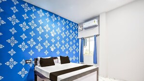 Quarto com cama, parede estampada em azul, aparelho de ar condicionado e janela com cortinas.